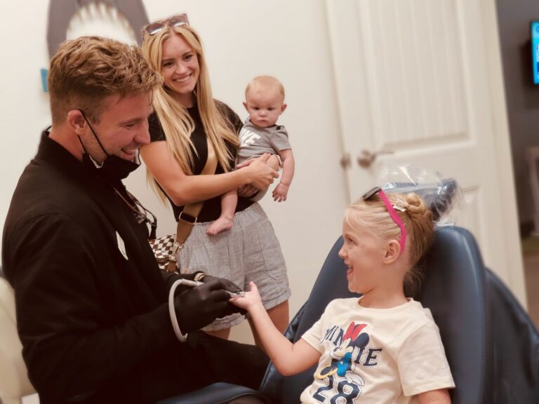 Dr. Austin Williams laughing with a young patient while her mom and baby brother watch